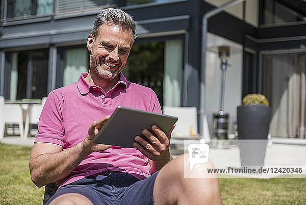 Smiling mature man sitting in garden of his home using a tablet