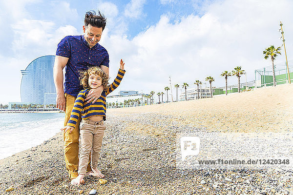 Spain Barcelona young boy with feet over his father on beach with pebbles