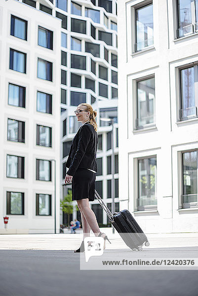 Mature businesswoman with suitcase walking in front of office buildings