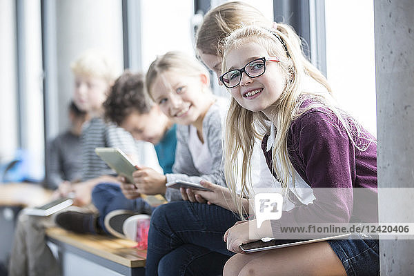 Smiling pupils with tablets on school corridor
