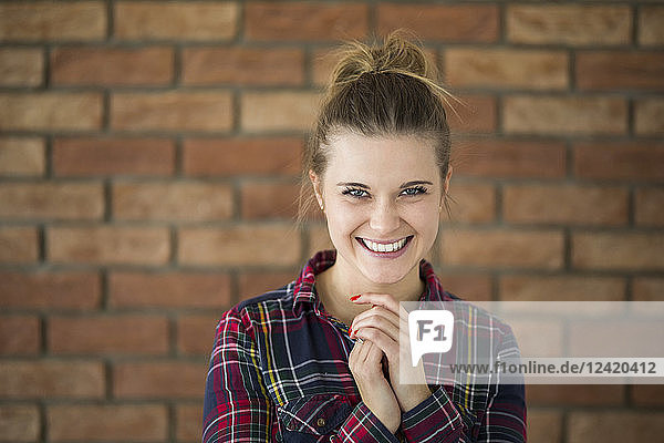 Portrait of laughing young woman in front of brick wall