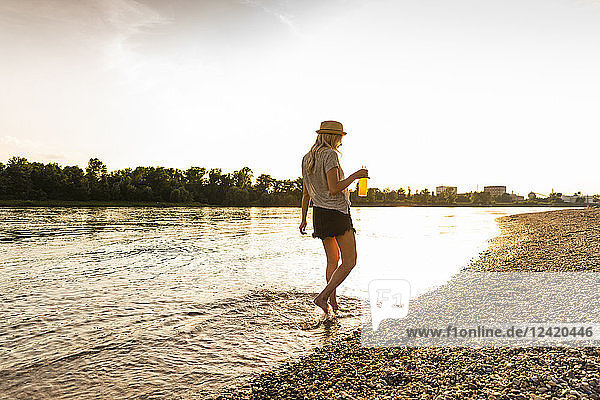 Young woman walking barefoot on riverside in the evening