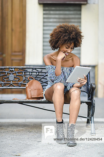 Young woman sitting on bench in the city using tablet