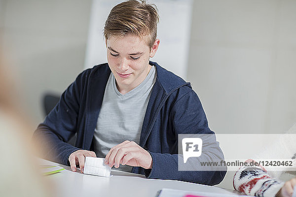 Teenage boy folding note in class