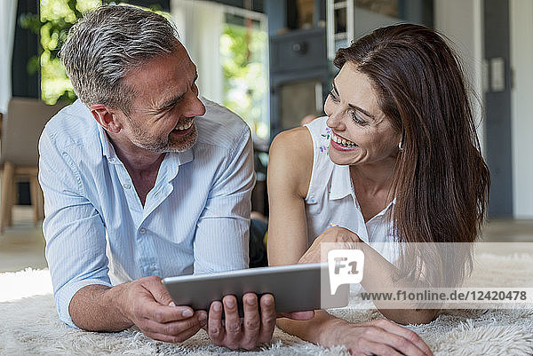 Happy couple lying on carpet at home sharing a tablet