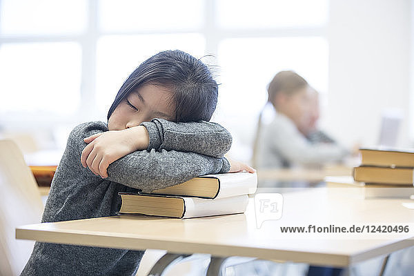 Schoolgirl sleeping on stack of books on table in school