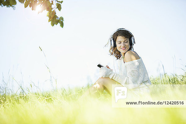 Smiling young woman with earphones and smartphone listening to music
