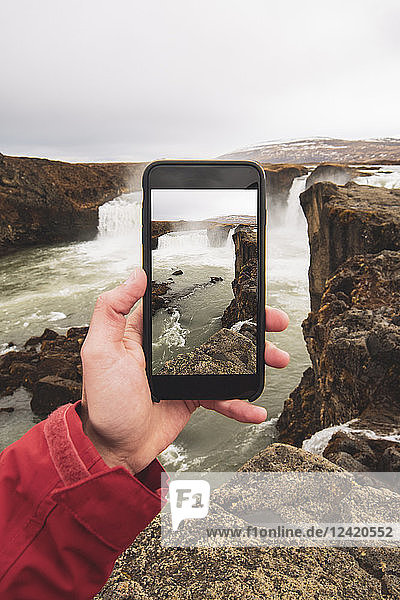 Iceland  hand holding cell phone with picture of Godafoss waterfall