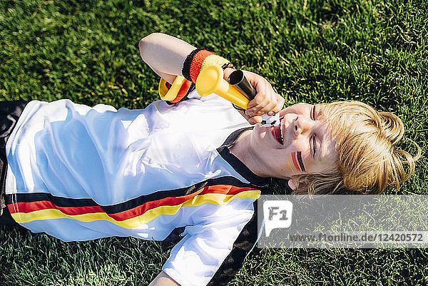 Boy in German soccer shirt lying on grass  blowing horns