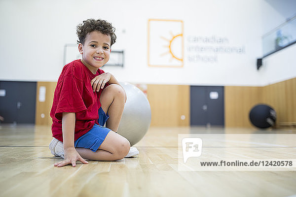 Portrait of smiling schoolboy with gym ball in gym class