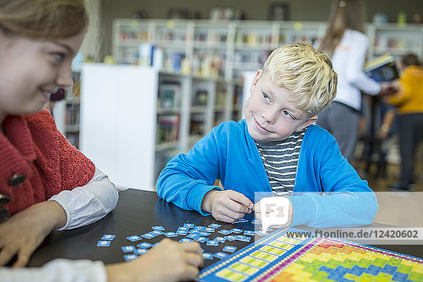 Pupils playing a board game in school library smiling at each other
