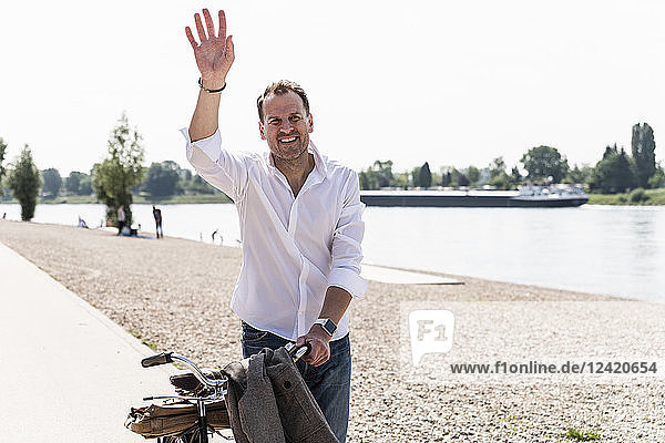 Mature man with bike waving at Rhine riverbank