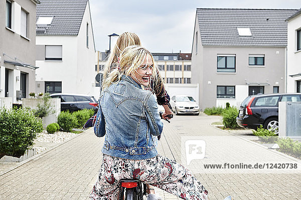 Two happy young women riding bicycle together on one bike