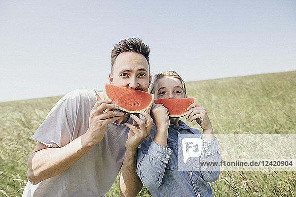 Portrait of young man and boy on a field holding watermelons