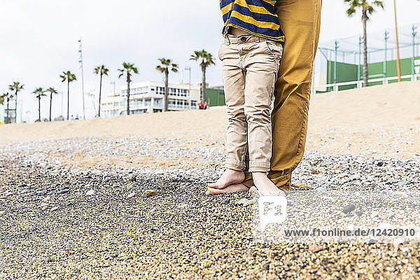 Spain  Barcelona  young boy with feet over his father on beach with pebbles