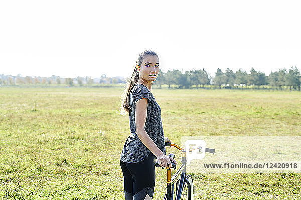 Sportive young woman with bicycle on a meadow
