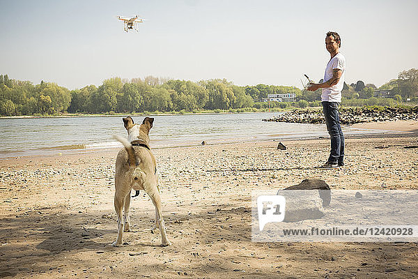 Man with a dog flying drone at a river