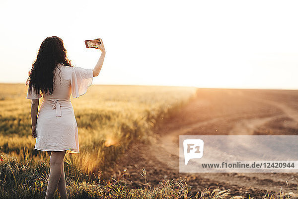 Young woman standing by field  taking selfie at sunset
