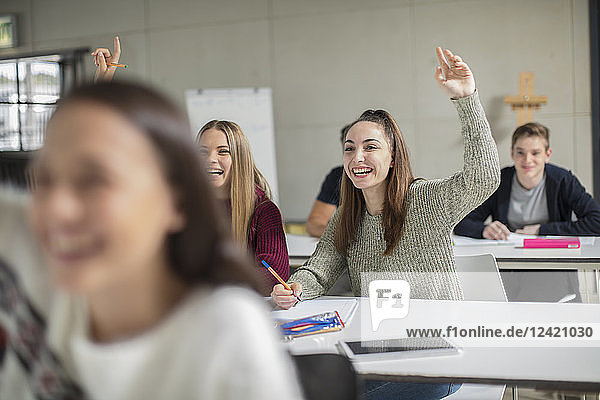 Happy teenage girls raising hands in class