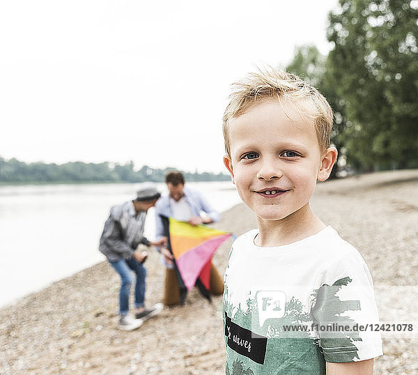 Portrait of smiling boy with father and brother holding kite at the riverside