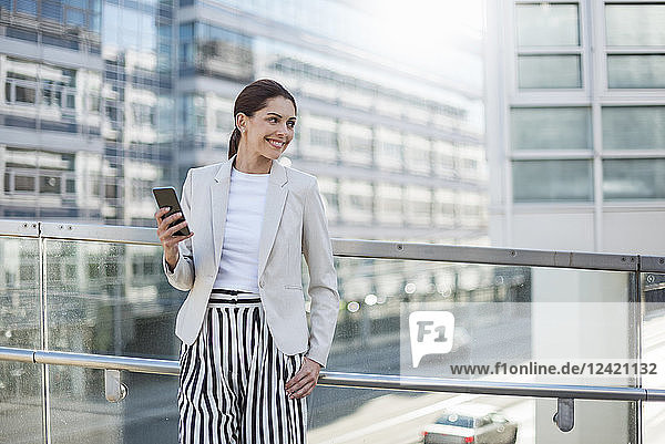 Portrait of smiling businesswoman with cell phone waiting on bridge