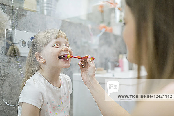Mother brushing teeth of her daughter in bathroom