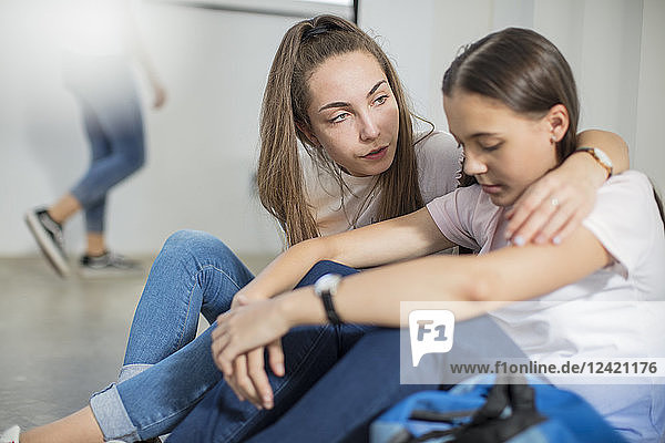 Teenage girl consoling sad friend in school