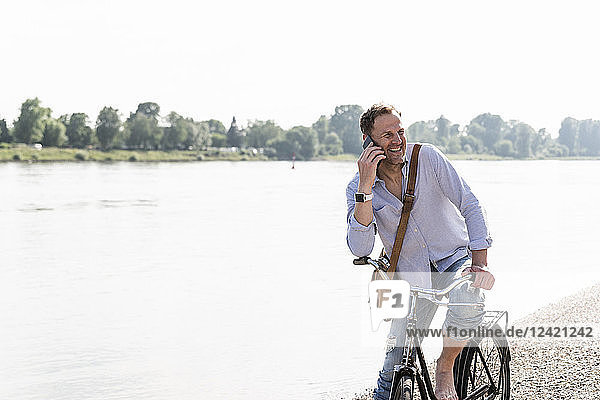 Mature man with bike using smartphone at Rhine riverbank