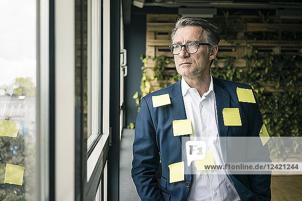 Serious mature businessman covered with sticky notes looking out of window