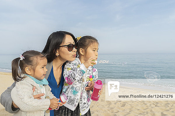 Mother with two daughters blowing soap bubbles on the beach
