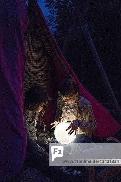 Two girls sitting in tipi  holding lamp as moon