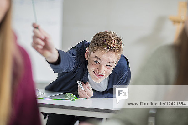 Smiling teenage boy passing a note in class