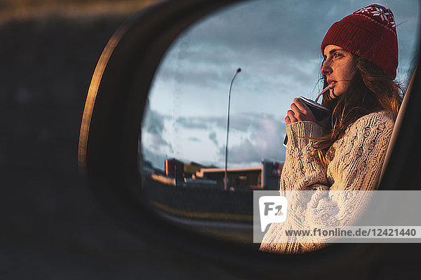 Iceland  young woman with coffee to go at sunset  mirrored in wing mirror