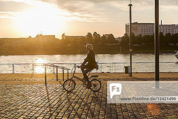 Senior woman riding city bike at the riverside at sunset