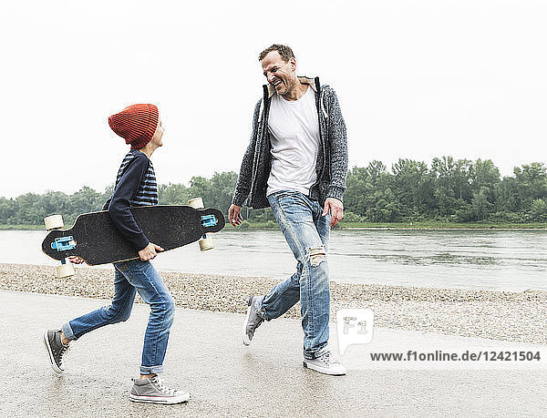 Happy father and son with skateboard at the riverside