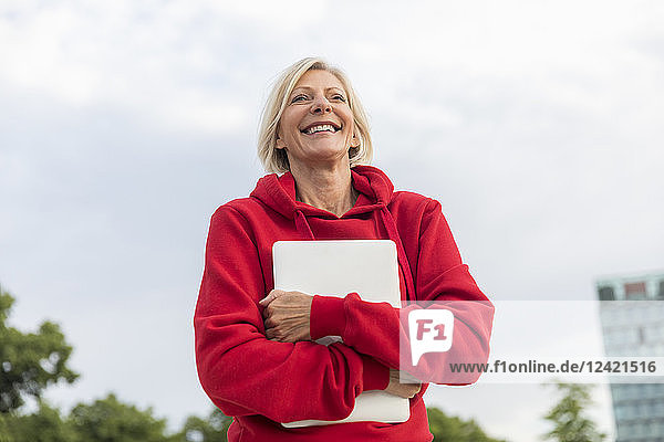 Happy senior woman wearing red hoodie holding laptop outdoors