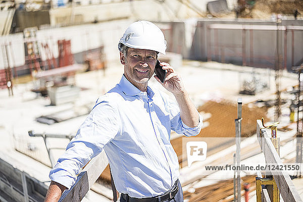 Smiling man wearing hard hat on cell phone on construction site