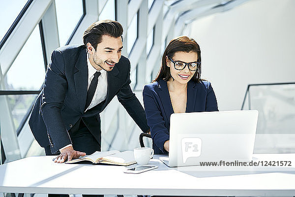 Smiling businesswoman and businessman using laptop at desk in modern office