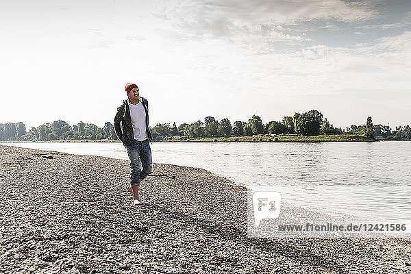 Mature man with red beanie walking at Rhine riverbank