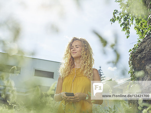 Smiling young woman with cell phone and earphones outdoors