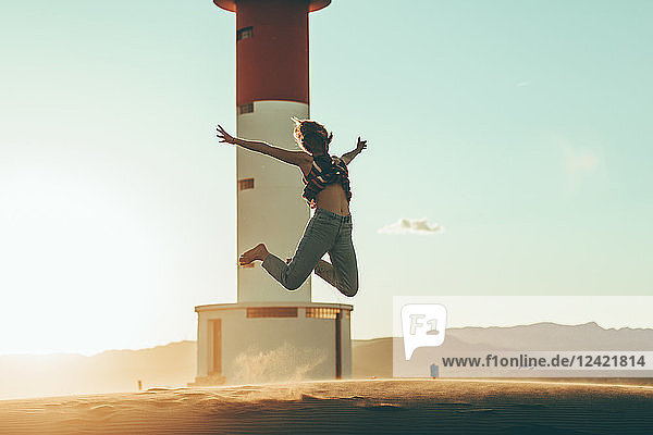 Young woman jumping in desert landscape at lighthouse