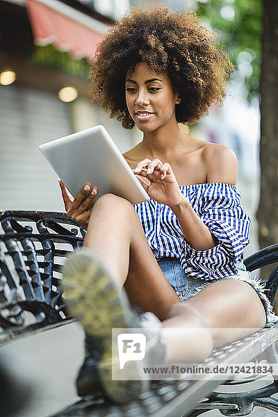 Portrait of young woman with curly hair sitting on bench using tablet