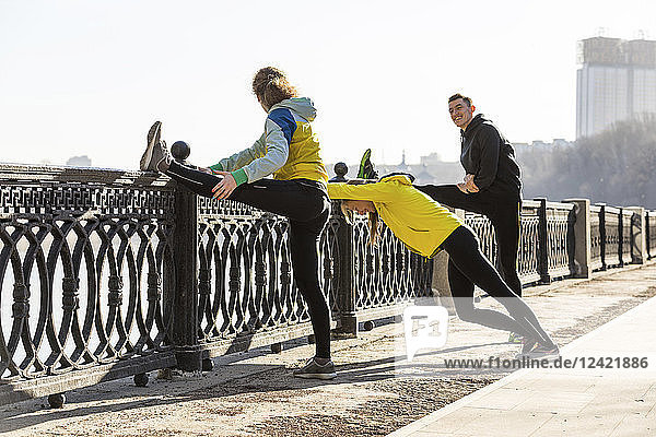 Friends doing stretching exercise on railing in the city