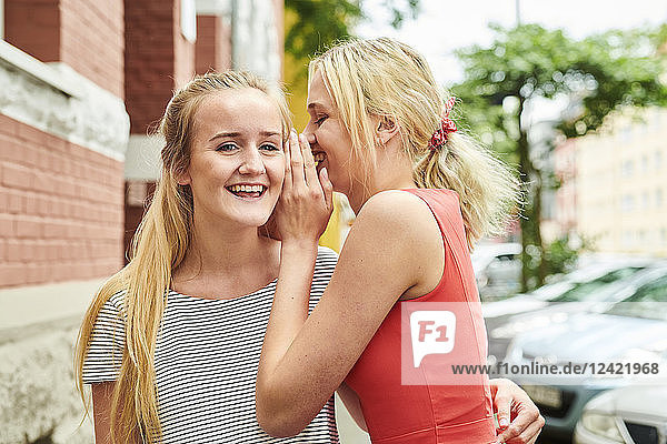 Two happy young women in the city whispering