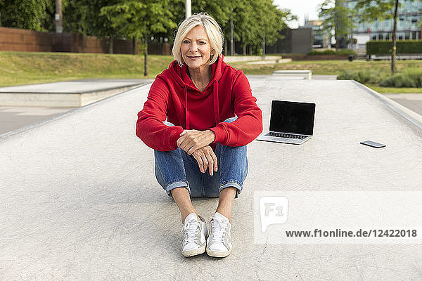 Senior woman wearing red hoodie sitting outdoors with laptop