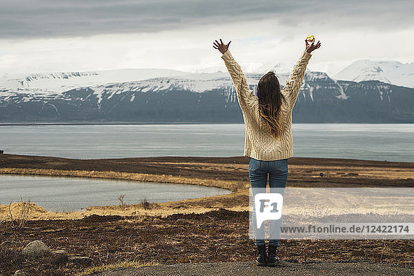 Iceland  woman standing at lakeside with raised arms
