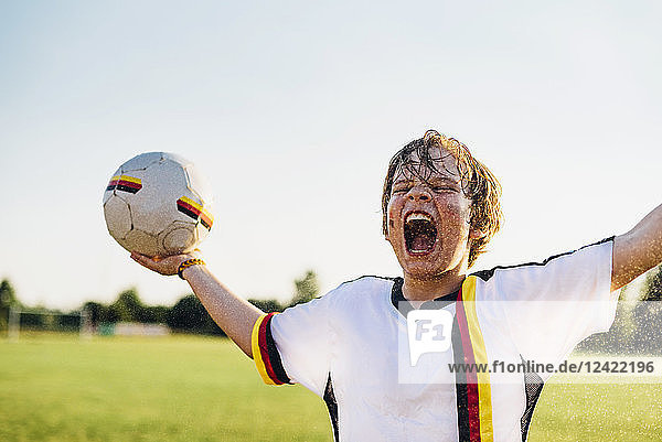 Boy wearing German soccer shirt screaming for joy  standing in water splashes