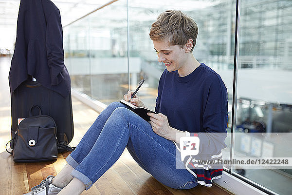 Blond businesswoman sitting on ground  writing in notebook