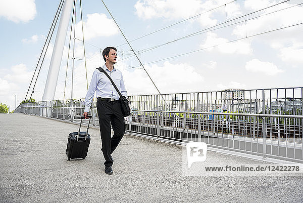 Businessman in the city with rolling suitcase crossing a bridge