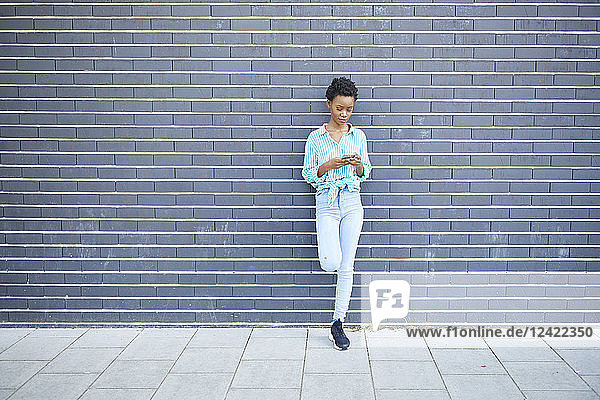 Woman standing in front of grey facade using cell phone